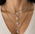 Gold necklaces with various pendants on a person wearing a beige top.