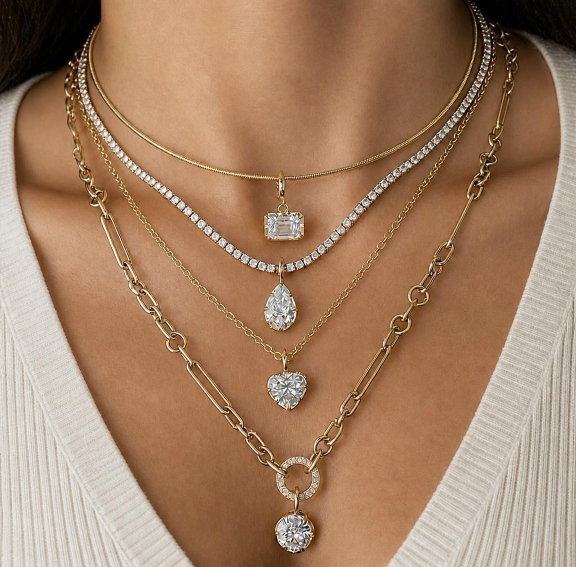 Gold necklaces with various pendants on a person wearing a beige top.