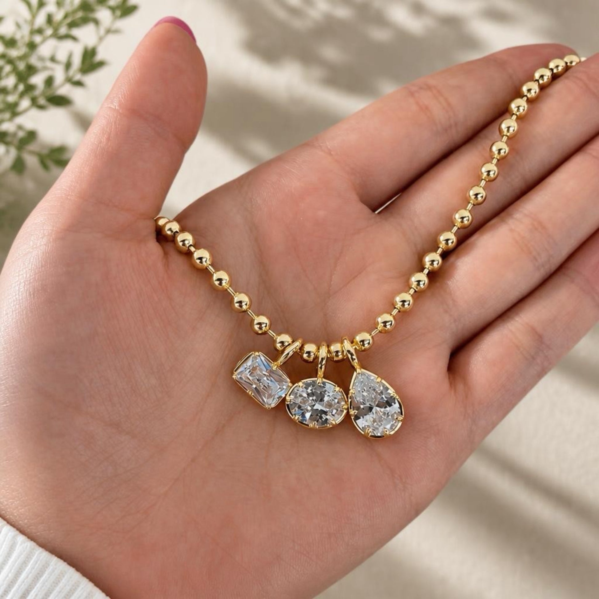 Gold necklace with pendant held in a hand against a neutral background